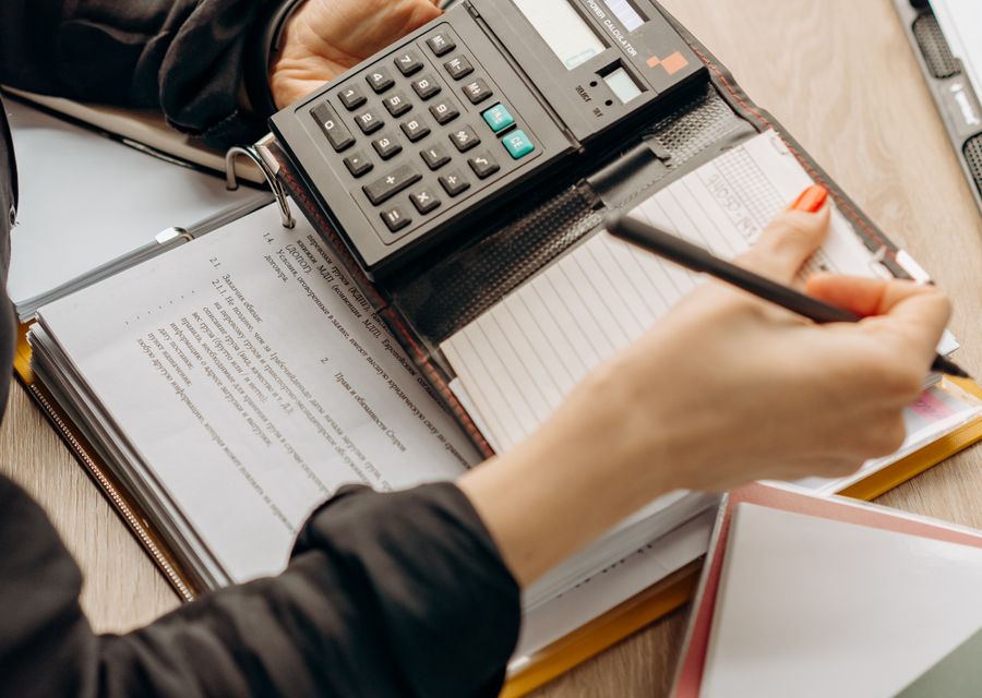 يدان تحسبان الأقساط على آلة حاسبة فوق مستندات مالية على مكتب